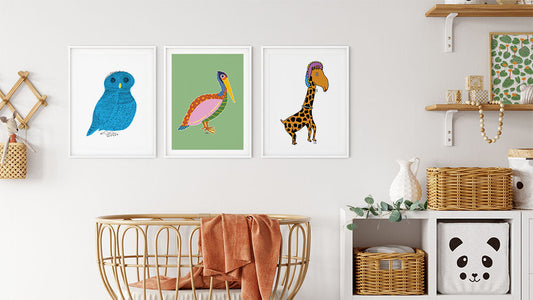 Framed animal art prints of an owl, pelican, and giraffe displayed above a crib in a modern nursery with natural wood and woven decor.