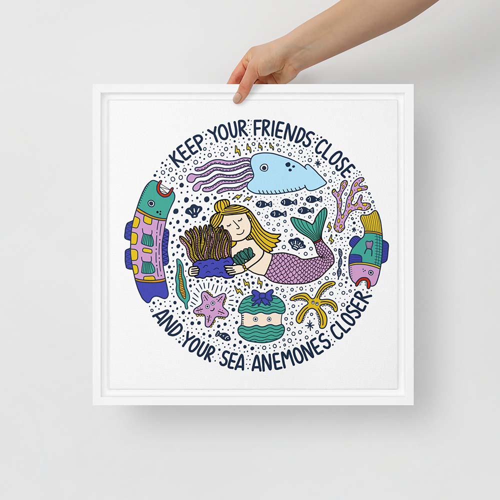 Hand holding artwork of mermaid hugging sea anemone surrounded by colorful ocean creatures with the phrase “Keep your friends close and your sea anemones closer” – framed square canvas wall art
