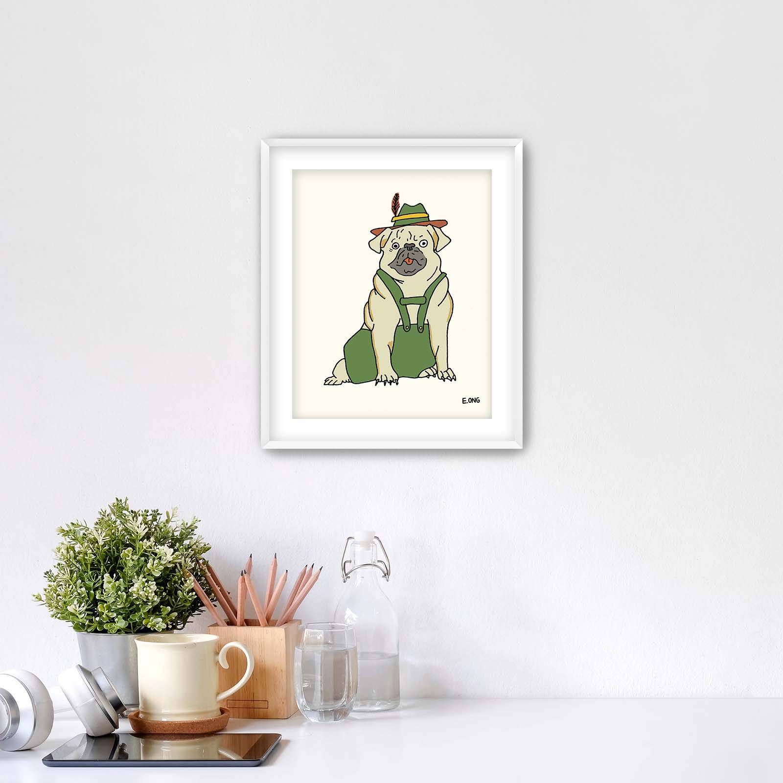 Pug in lederhosen art print by Erwin Ong displayed in a white frame above a minimalist desk with greenery and stationery – whimsical dog wall art for nursery or home office.